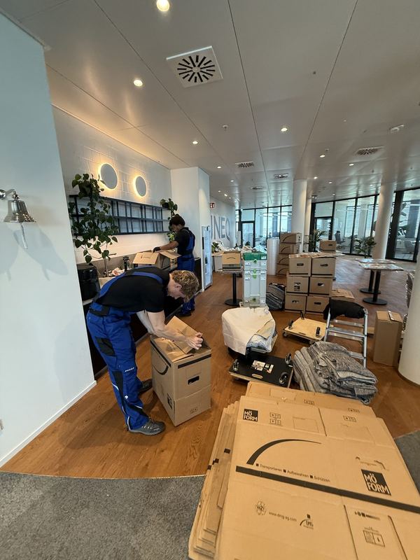 Einpacken an den Arbeitsplätzen In einem Großraumbüro verpackt ein Mitarbeiter Kartons, auf dem Parkett liegen zusammengefaltete Kartonagen neben gestapelten Kisten
