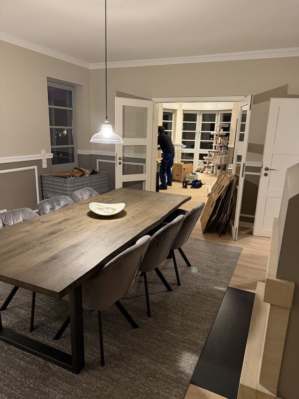 Ein eingeräumtes Esszimmer mit gedecktem Tisch, im Nebenraum werden leere Kartons zusammengefaltet