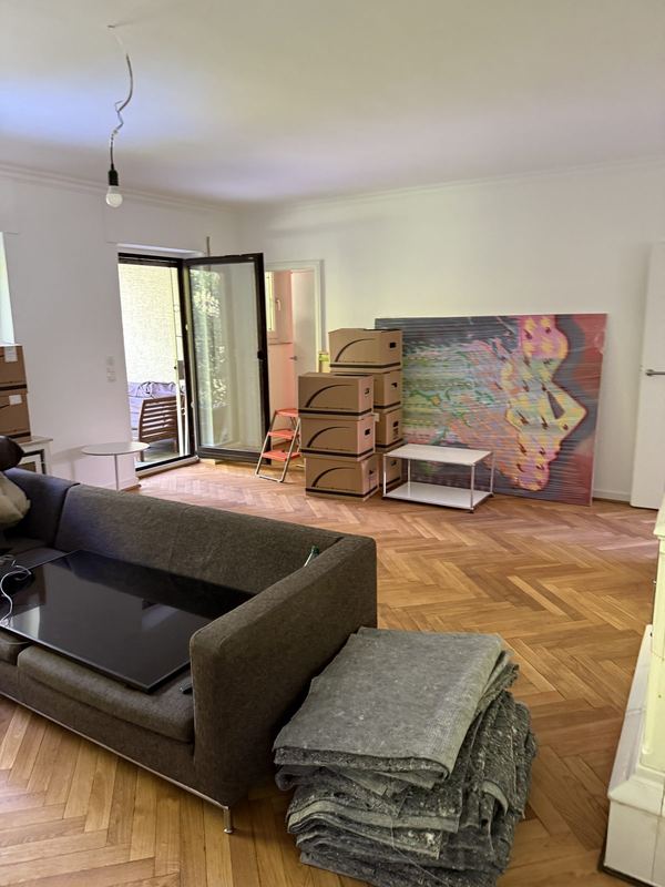 Ein Wohnzimmer mit Kartonstapeln entlang der Wand und zusammengefalteten Umzugsdecken