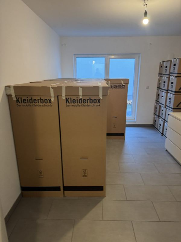 Zwei Kleiderboxen und gestapelte Kartons in einem noch leeren Zimmer