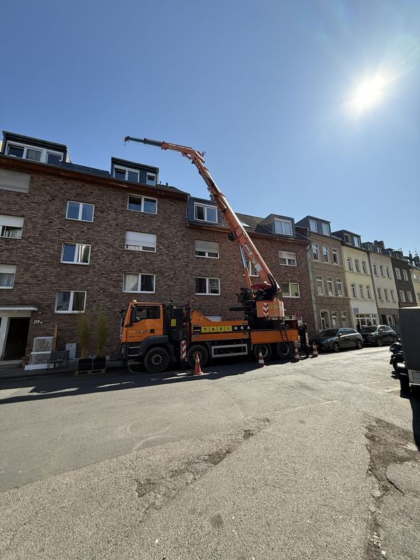 Ein orangefarbener Kranwagen mit ausgefahrenem Ausleger und Warnkegeln in einer Wohnstraße