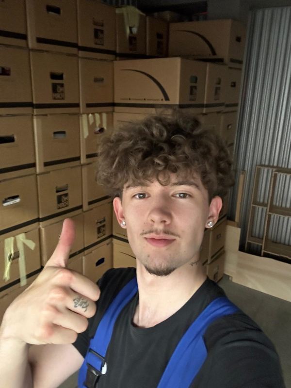 Ein Kollege steht vor einer Wand aus gepackten und beschrifteten Umzugskartons