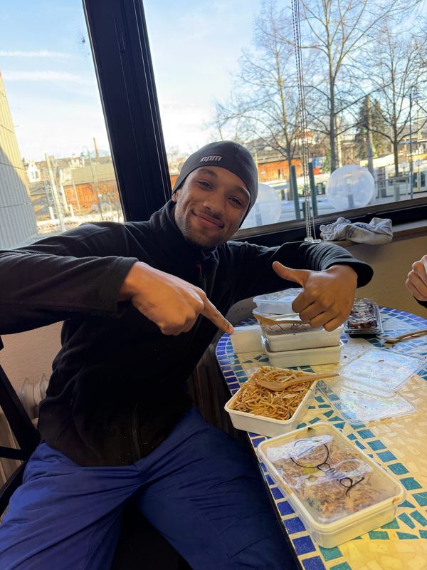Ein Kollege sitzt in der Mittagspause am Tisch und zeigt auf sein Essen