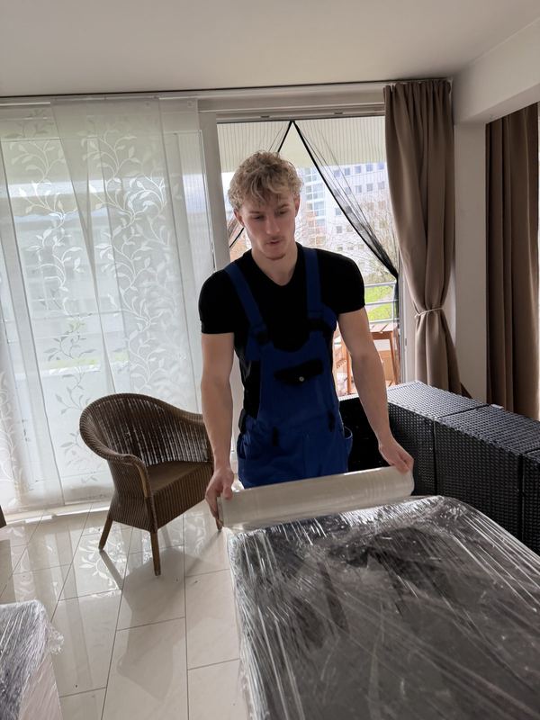 Ein Kollege wickelt in einer Wohnung Stretchfolie um ein Möbelstück