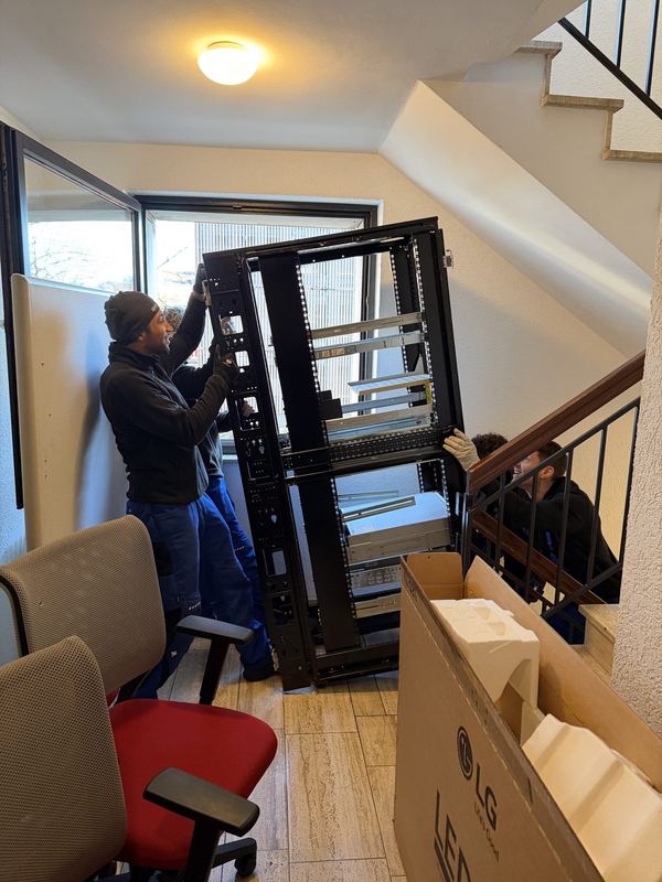 Drei Kollegen tragen einen offenen Serverschrank durch ein Treppenhaus nach unten