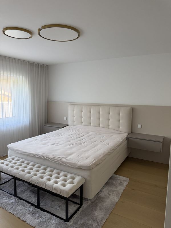 Ein helles Schlafzimmer mit fertig aufgebautem Boxspringbett und einer Sitzbank am Fußende