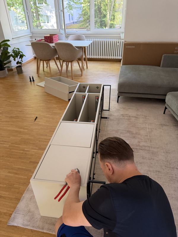 Von oben fotografiert: ein Monteur befestigt Beschläge an einem flach liegenden Sideboard