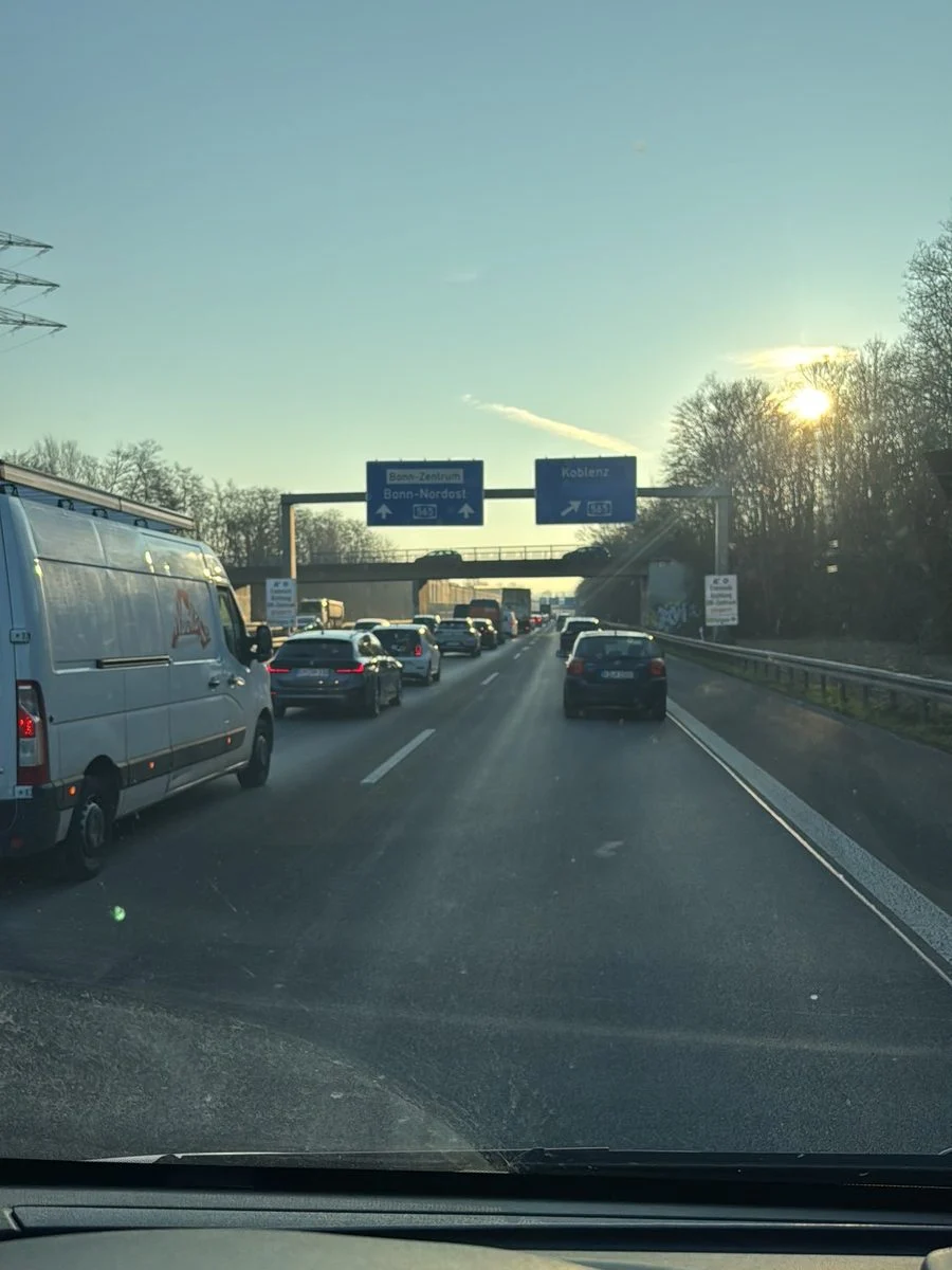 Durch das Autofenster blickt man auf einen Stau auf der Autobahn, direkt voraus fährt ein LKW.