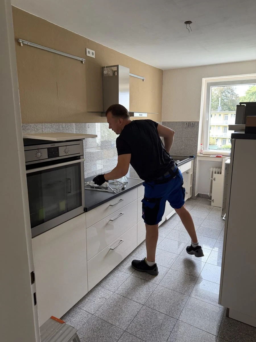 Ein Mitarbeiter montiert ein Kücheneinbaugerät, die Aufnahme zeigt ihn von hinten bei der Arbeit.
