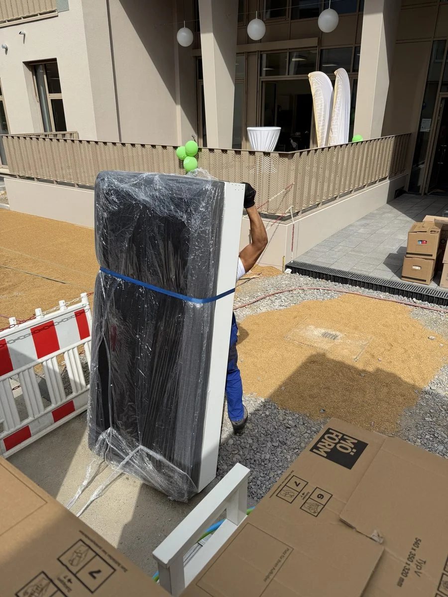 Ein in Folie verpacktes Gerät wird vorsichtig eine Treppe hinauf in die obere Etage getragen.