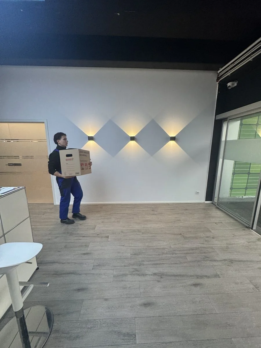 Ein Mitarbeiter trägt einen Karton durch einen leeren, offenen Loft-Raum mit viel Platz.