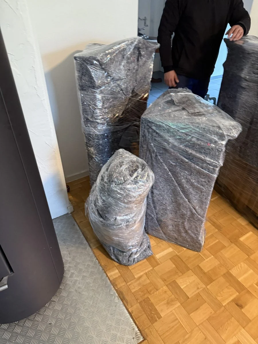 Ein Mitarbeiter steht mit dem Rücken zur Kamera neben verpackten Gegenständen am Kamin eines Wohnzimmers.