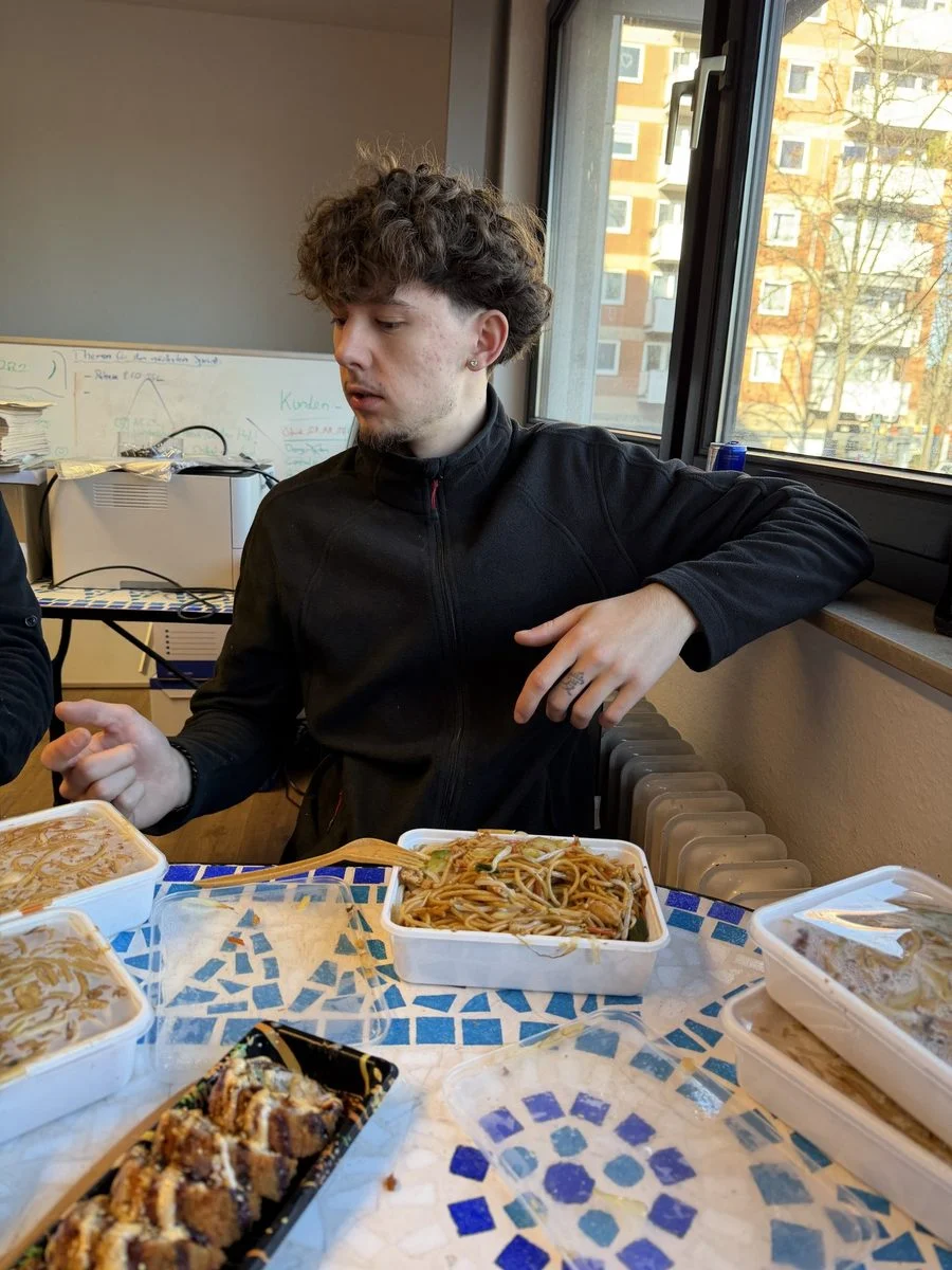 Ein Mitarbeiter sitzt am Tisch und isst in der Pause gemeinsam mit dem übrigen Team.