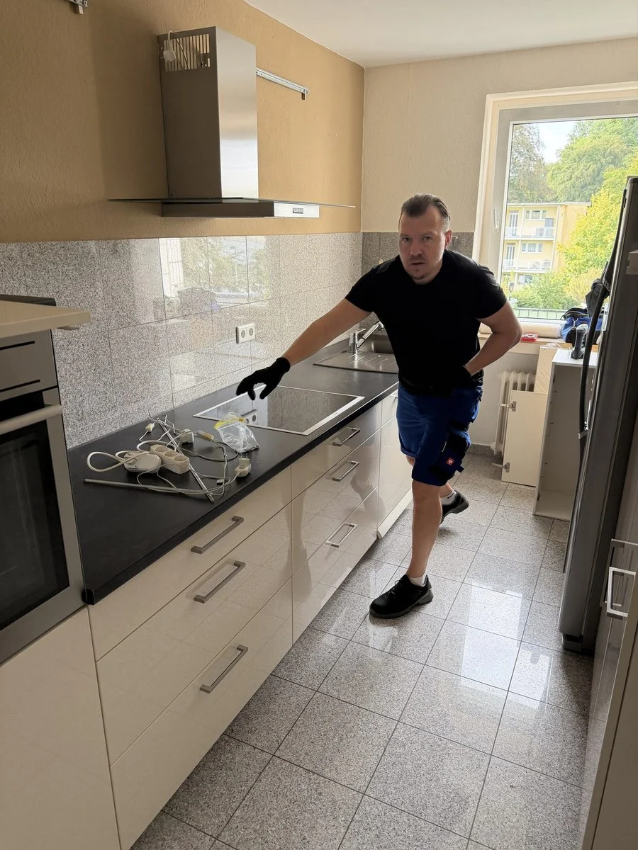 Ein Mitarbeiter beugt sich bei der Montage zu einem Küchenunterschrank und richtet ihn sorgfältig aus.