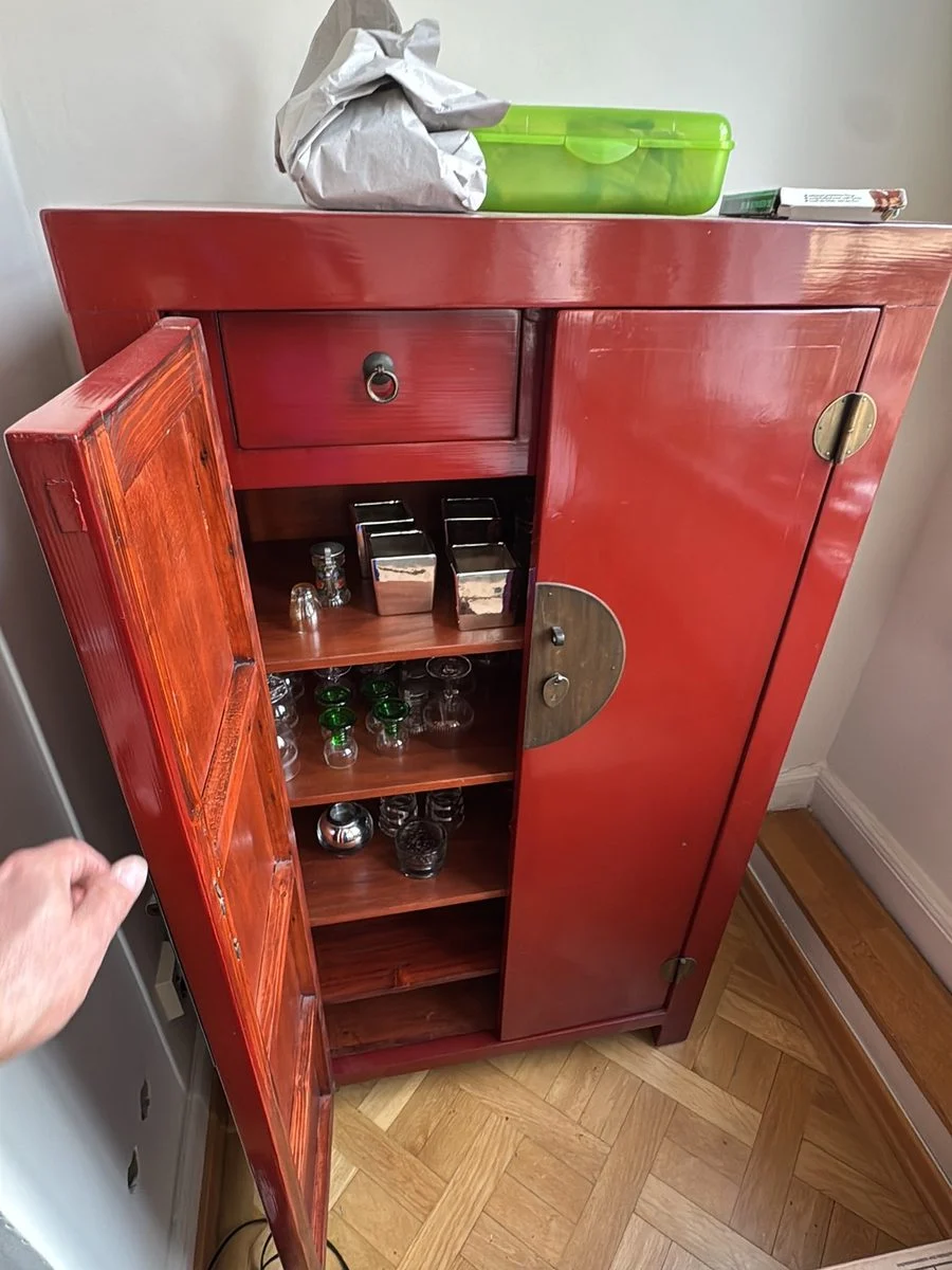 Ein roter antiker Lackschrank mit geöffneter Tür gibt den Blick auf die Innenseite frei.