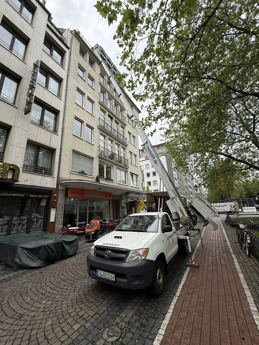 Der ausgefahrene Mast eines Möbellifts ragt weit über eine Baumallee hinaus nach oben.