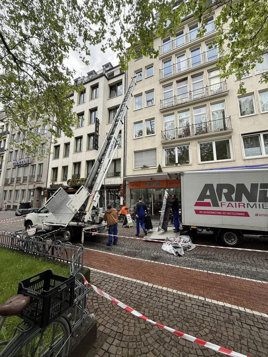 Ein Fahrzeug mit Möbellift steht auf der Straße vor einem Altbau und ist für den Einsatz bereit.
