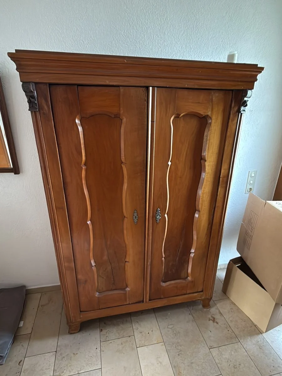 Ein antiker Holzschrank steht allein in einem Raum mit Steinboden und wartet auf die Demontage.