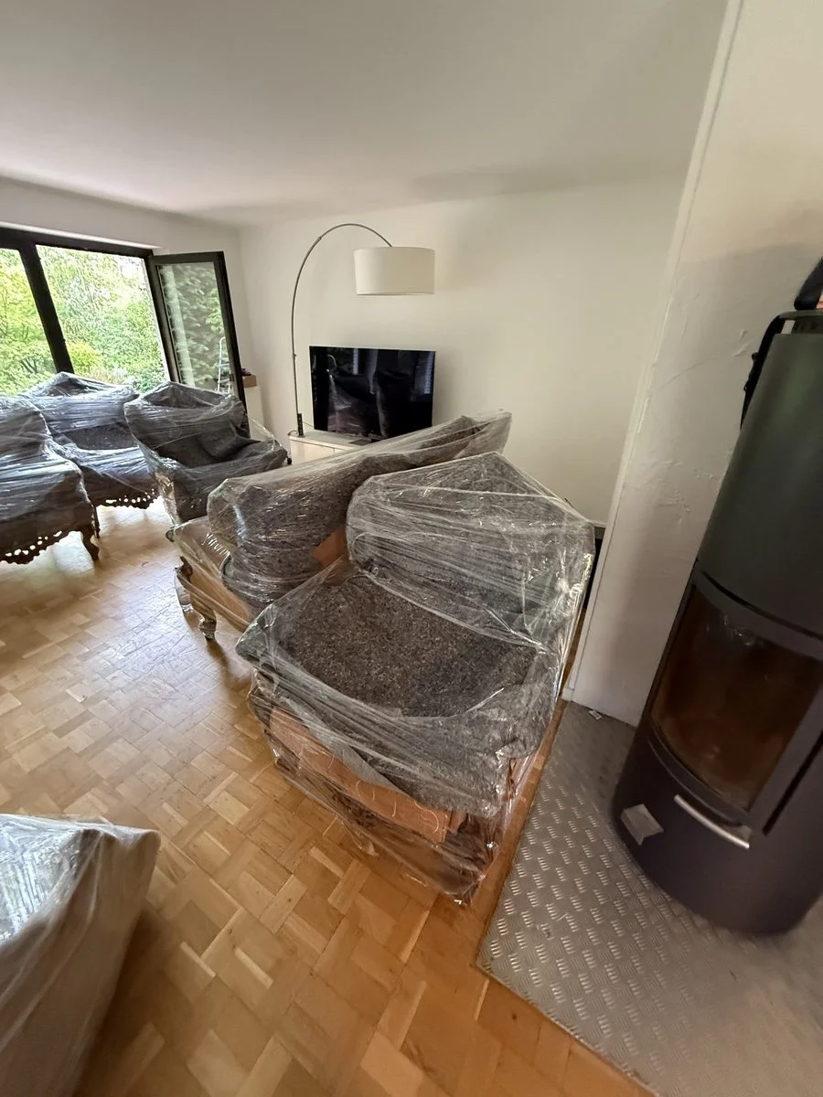 Mehrere in Folie eingepackte Sessel stehen in einem Wohnzimmer vor dem Kamin.