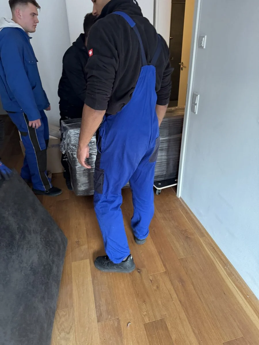 Umzugsunion Bergisch Gladbach, zwei Umzugshelfer in Arbeitskleidung tragen Kisten durch den Flur einer Wohnung nach draußen.