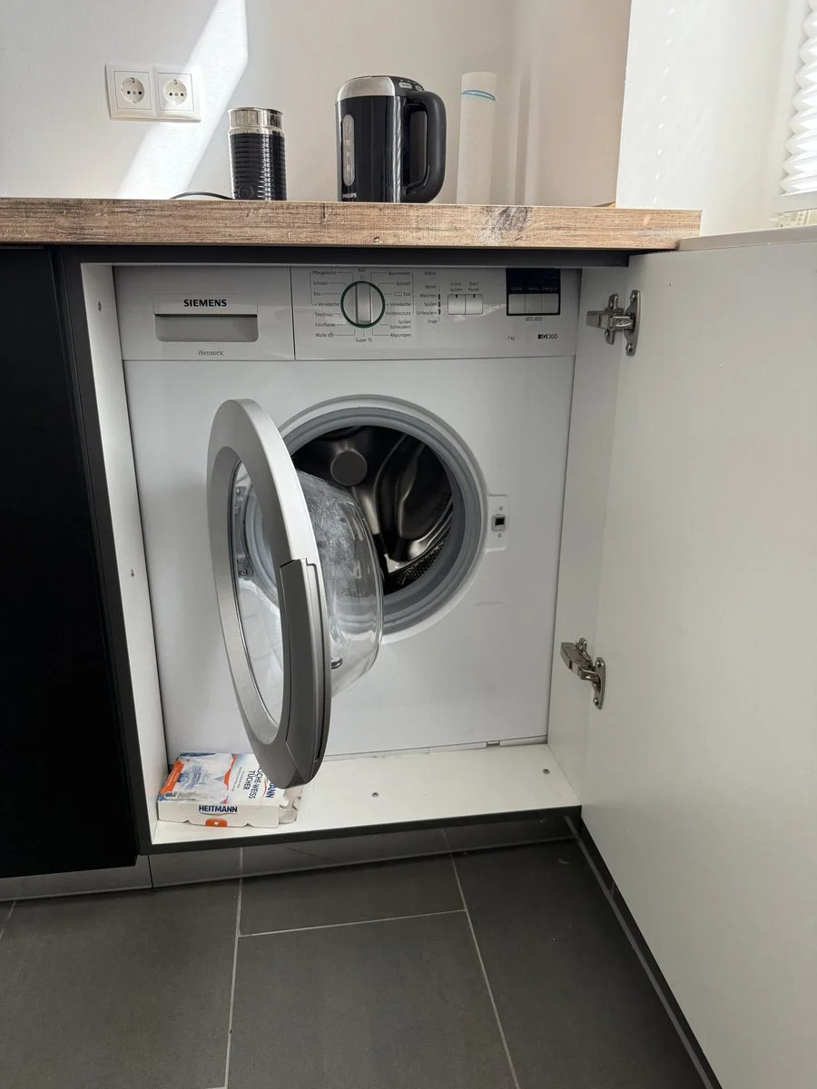 Eine in die Küche eingebaute Waschmaschine, bei der gerade der Wasseranschluss hergestellt wird.