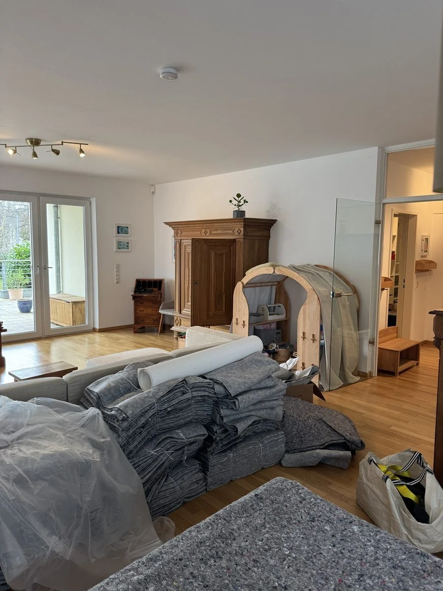 In einem Wohnzimmer steht ein antiker Schrank, die übrigen Möbel sind verpackt und stehen auf dem Parkett.