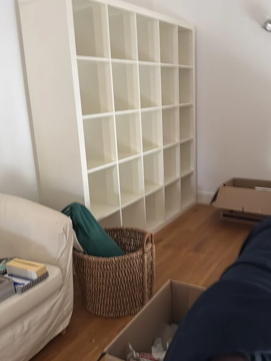 Ein weißes Würfelregal steht an der Wand, davor warten ein Sack und ein Umzugskarton auf das Tragen.